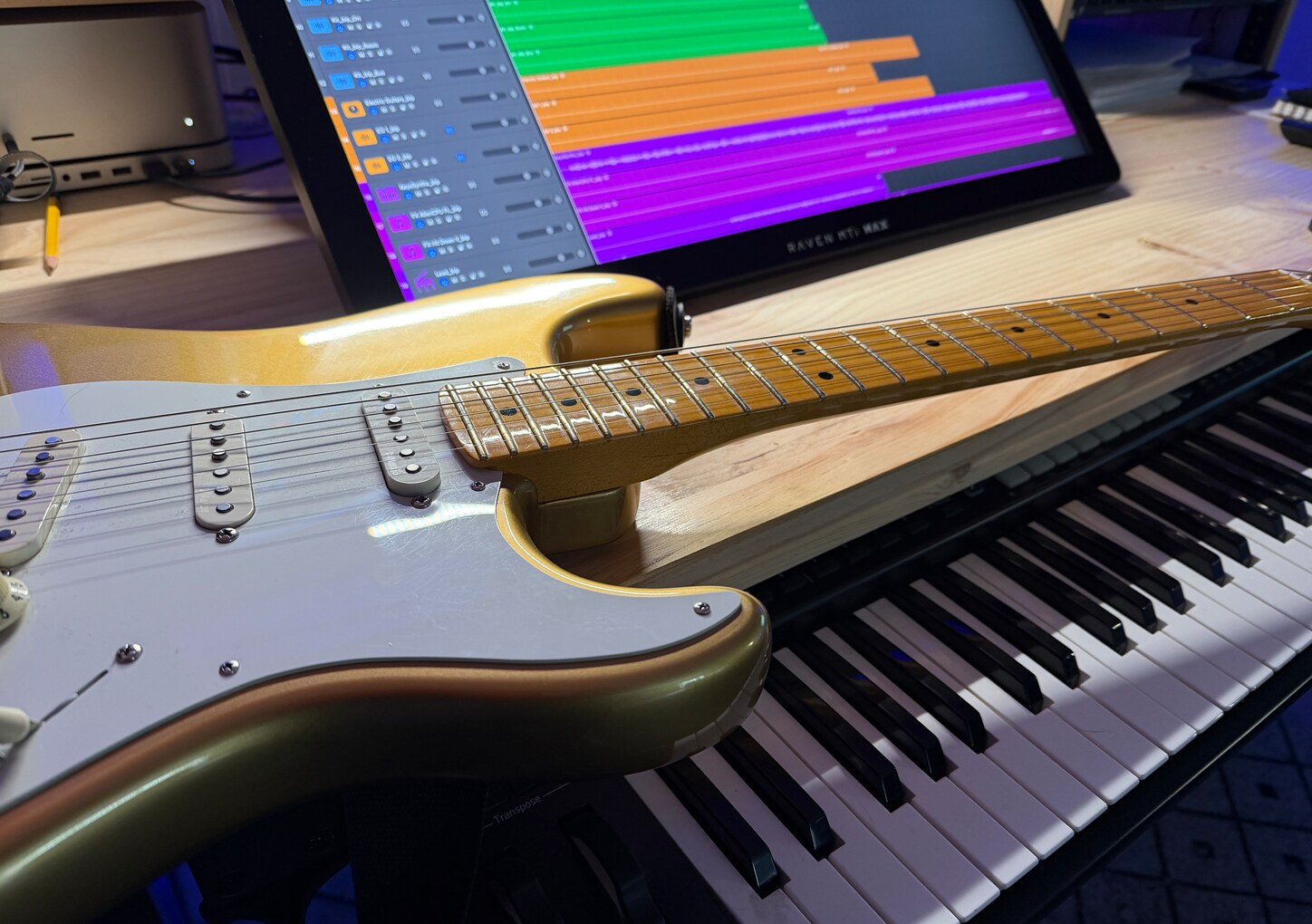 Gold electric guitar resting above a keyboard in Jamie Penner’s studio, with multitrack music software open on a screen behind it